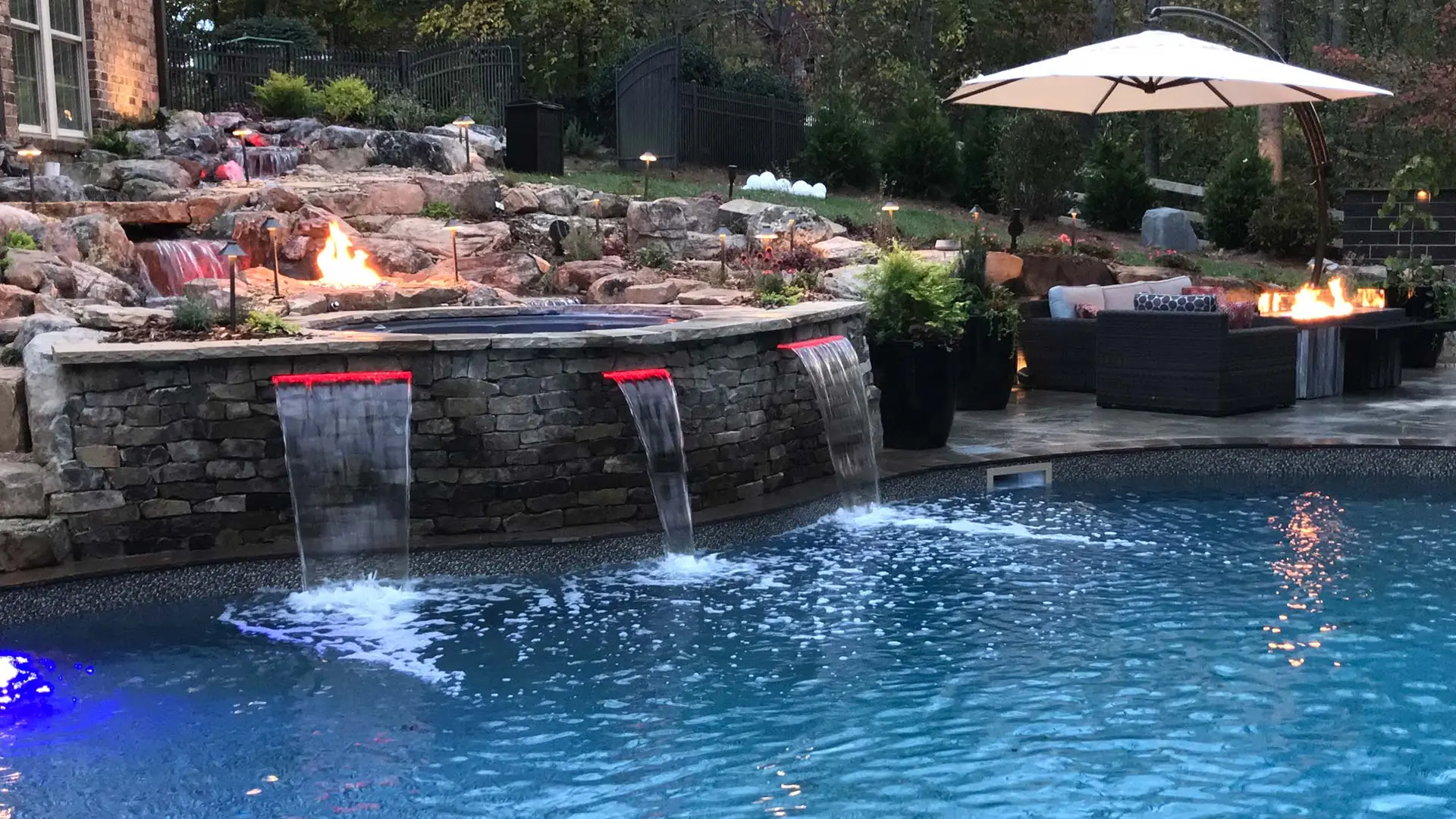 Natural rock landscaping with patio, fire pit, and water flowing into pool near Greensboro, NC.