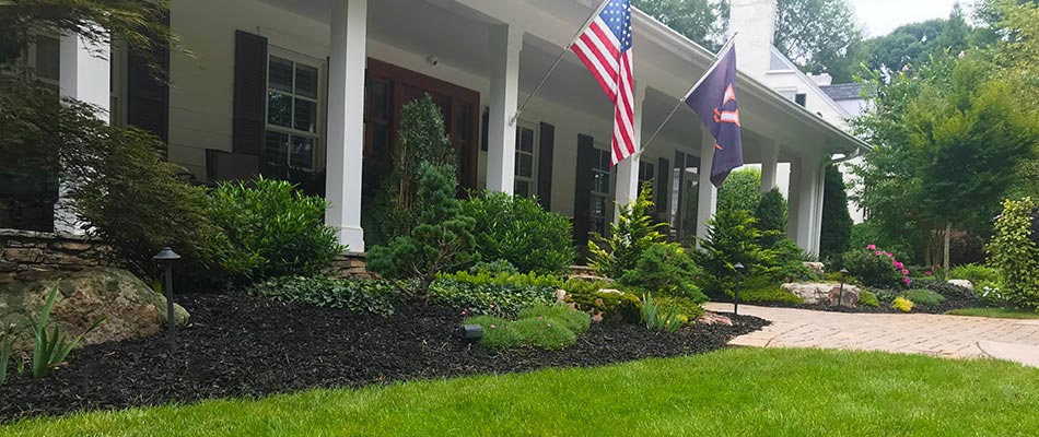 Dark mulch landscape bed with plantings and U.S. flag nearby in Winston-Salem, NC.