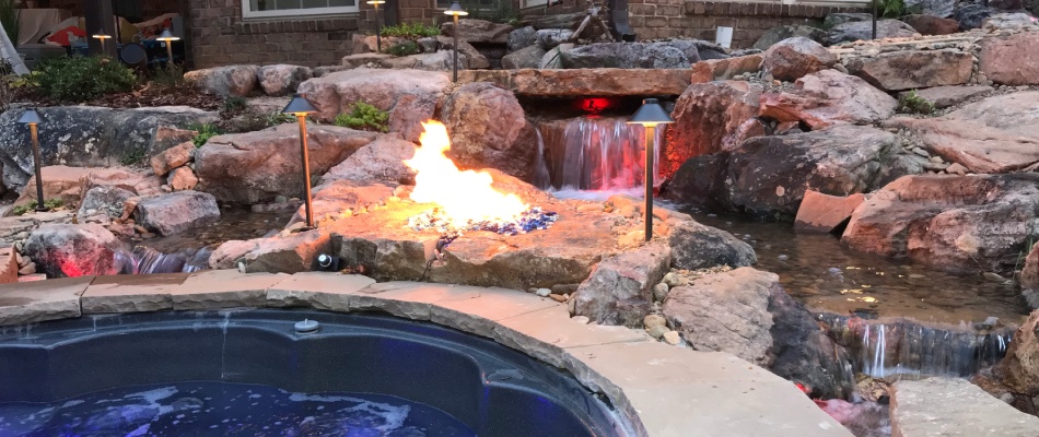 Upgraded hardscape with water feature and fire pit beside a pool deck in Summerfield, NC.