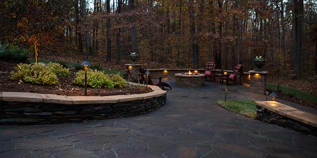 Large patio with seating and retaining walls near fire pit in Summerfield, NC.