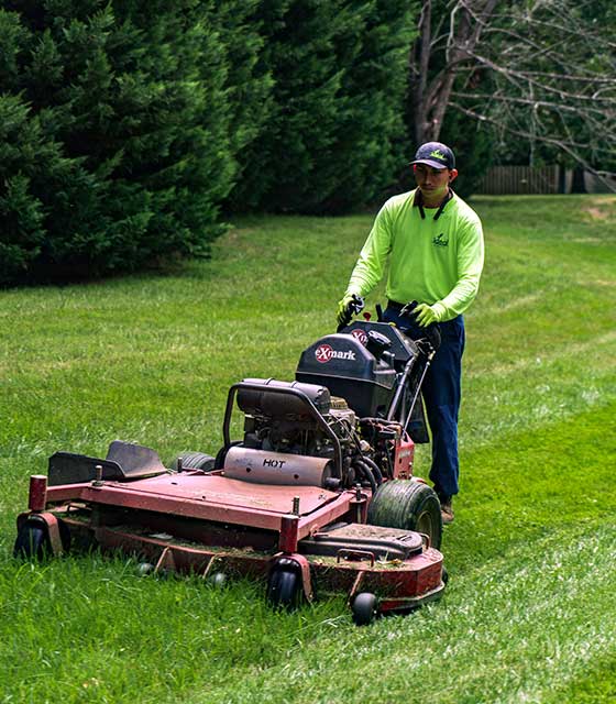 Lawn care worker mowing a large yard in Greensboro, NC.